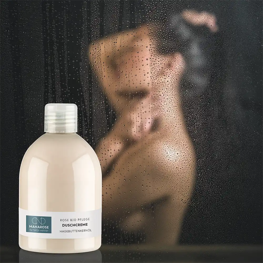 Eine Frau steht vor einer Dusche und hält eine Flasche Duschcreme Hagebuttenkernöl von Manarose Biokosmetik in der Hand.