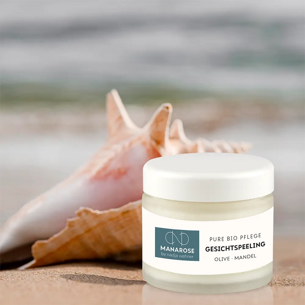 Ein Glas Gesichtspeeling Olive Mandel Creme von Manarose Biokosmetik am Strand.
