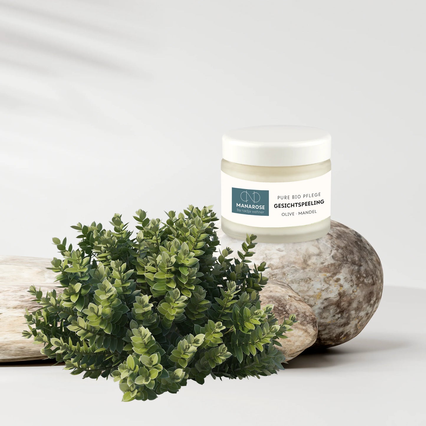 Ein Glas Manarose Biokosmetik Gesichtspeeling Olive Mandel Creme neben einer Pflanze.