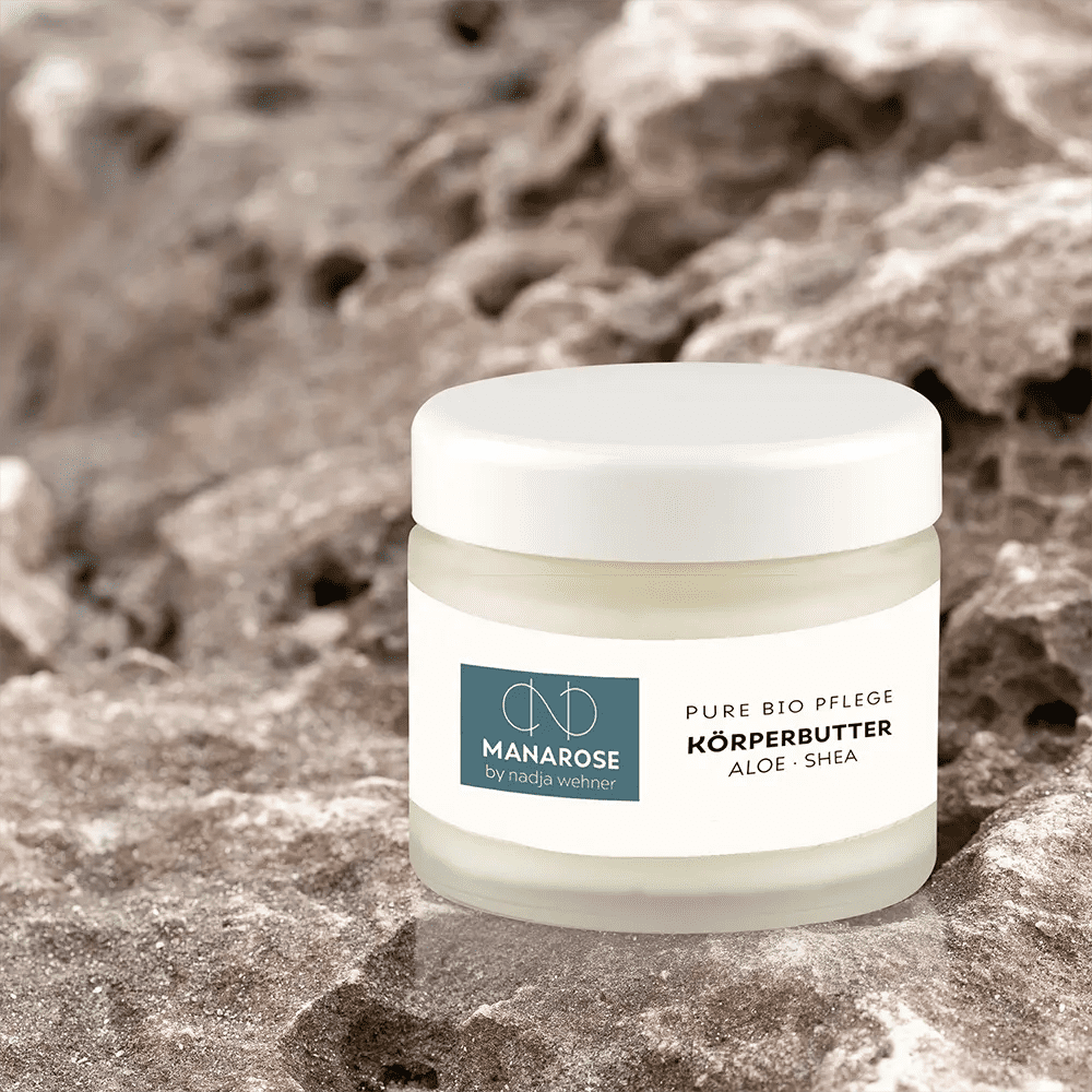Ein Glas Körperbutter Aloe Shea von Manarose Biokosmetik für trockene und empfindliche Haut auf einem Stein sitzend.