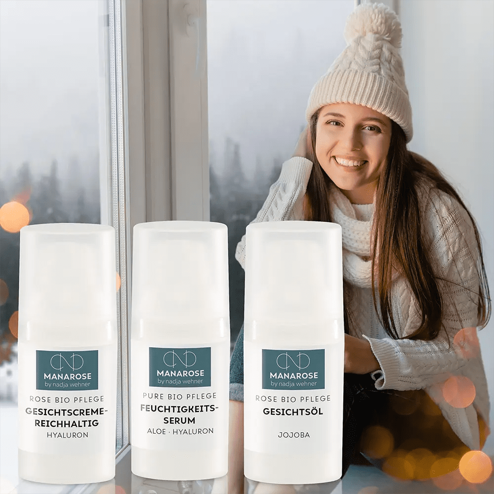 Eine Frau sitzt vor einem Fenster mit drei Flaschen Gesichtspflege Set - Winter Care von Manarose Biokosmetik.