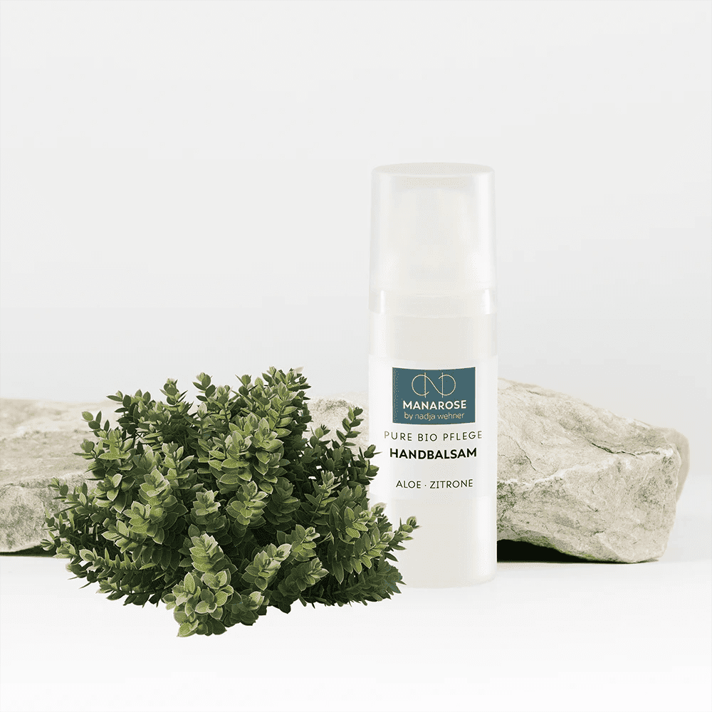 Eine Flasche Handbalsam Aloe Zitrone Gesichtsöl von Manarose Biokosmetik neben einer Pflanze und Steinen.