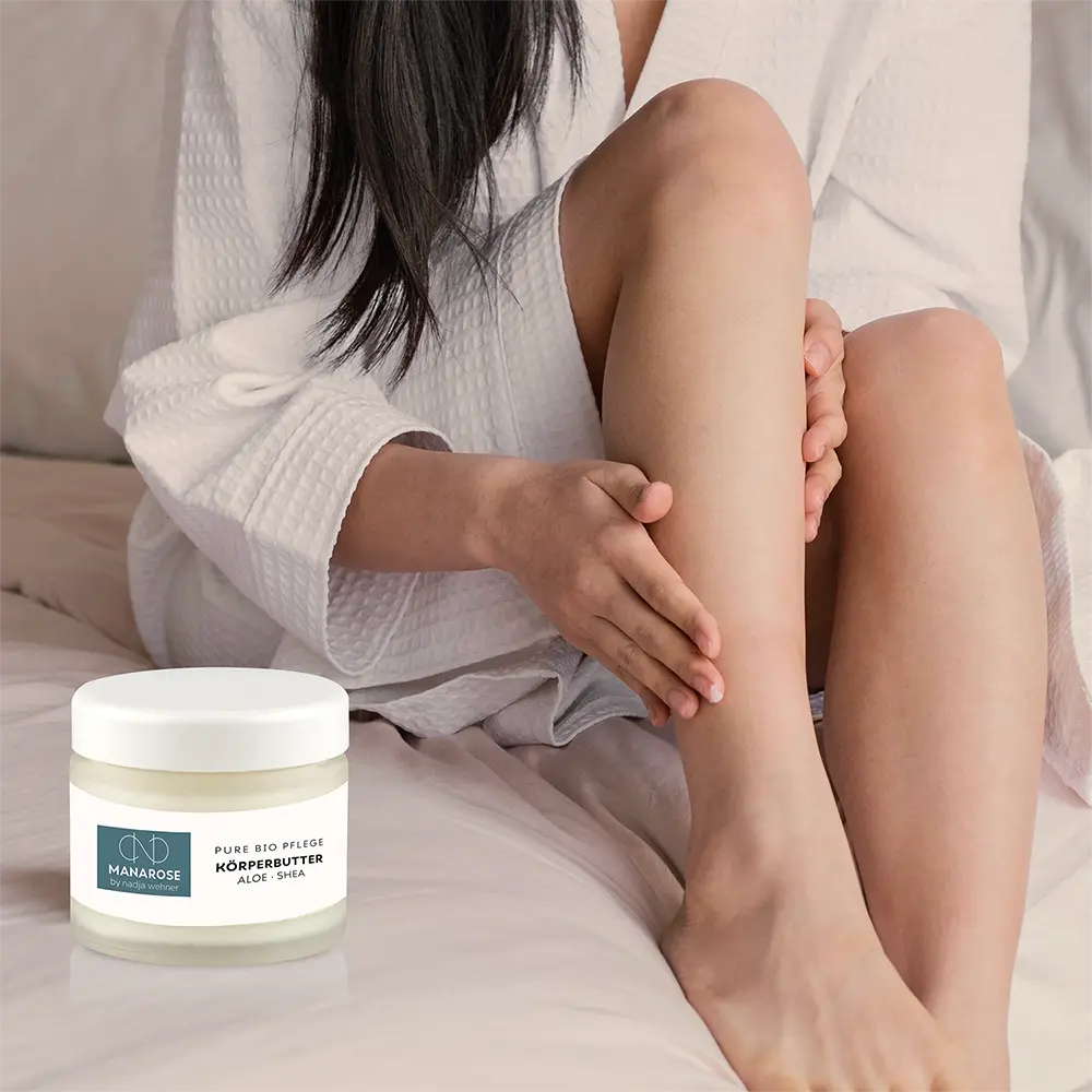 Eine Frau sitzt auf einem Bett mit einem Glas Körperbutter Aloe Shea von Manarose Biokosmetik für trockene und empfindliche Haut.