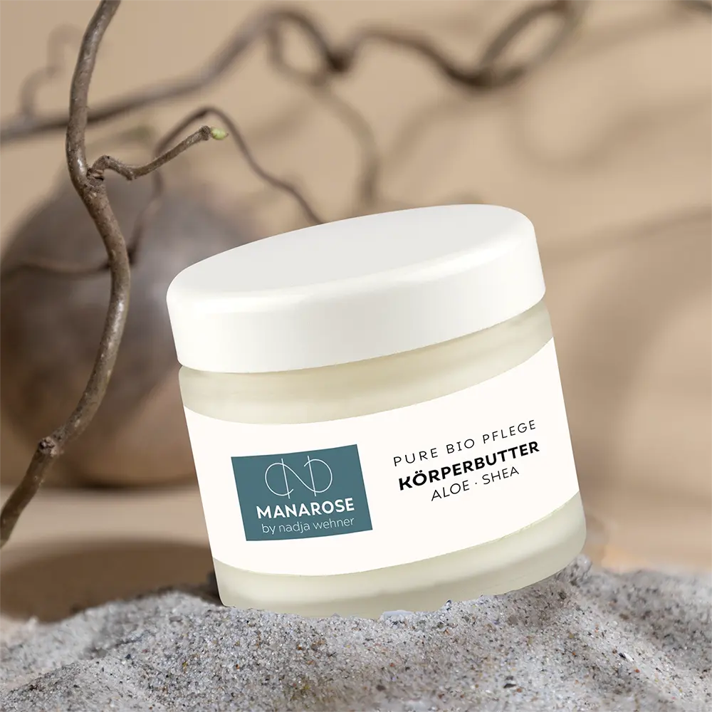 Ein Glas Manarose Biokosmetik Körperbutter Aloe Shea steht im Sand.