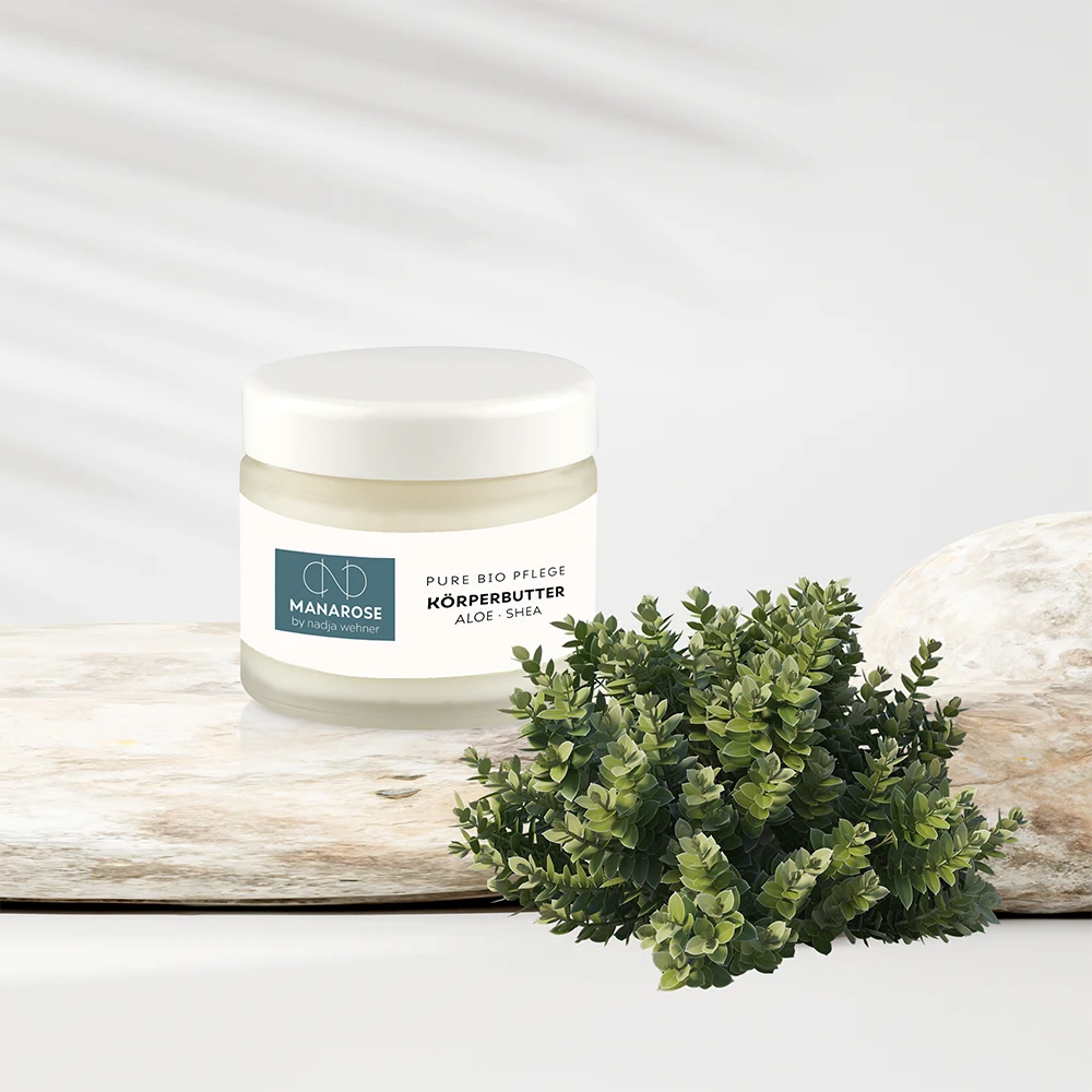 Eine Dosis Körperbutter Aloe Shea von Manarose Biokosmetik neben einer Pflanze.