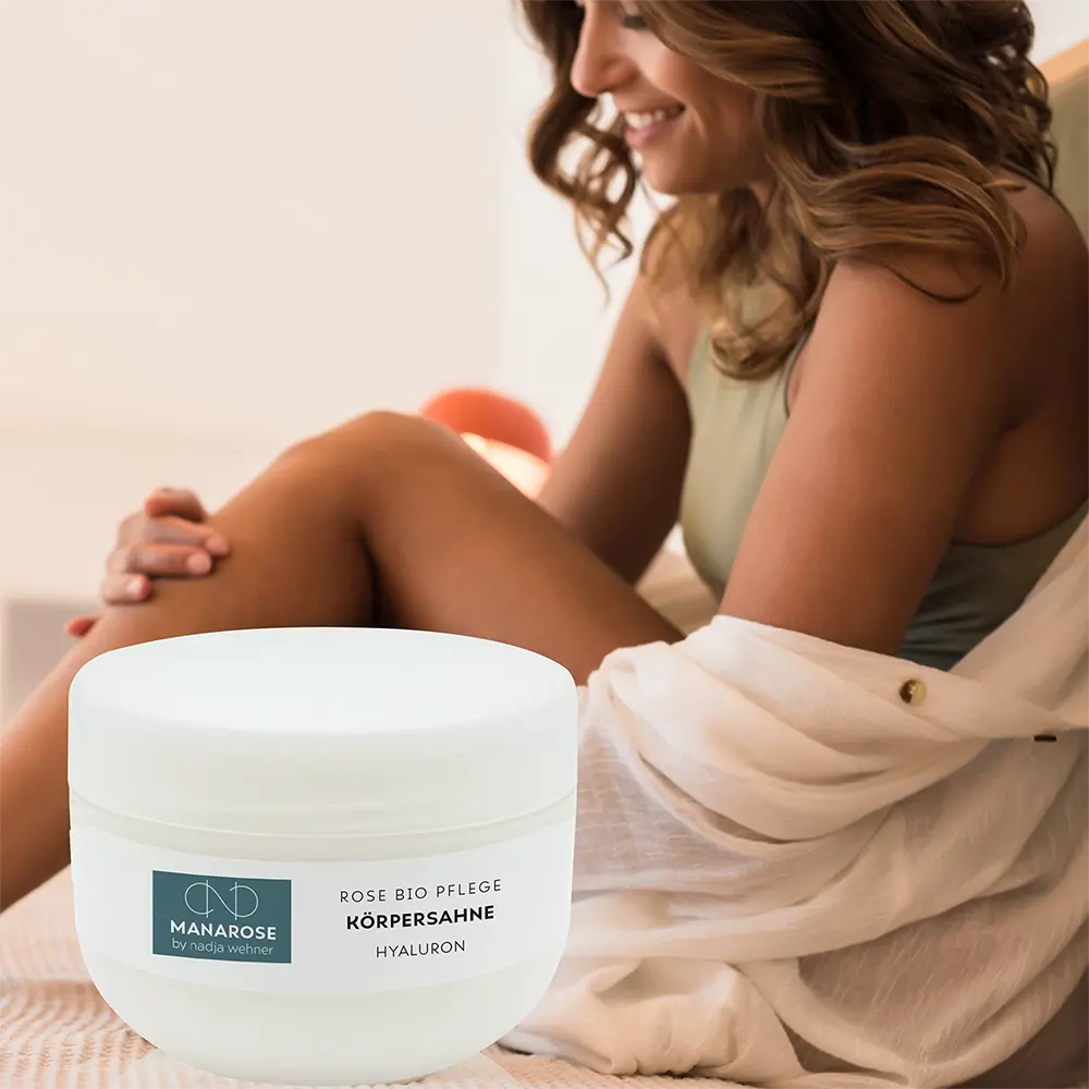 Eine Frau sitzt auf einem Bett und trägt Manarose Biokosmetik Körperahne Rose Hyaluron mit einem Hauch Rosenduft auf.
