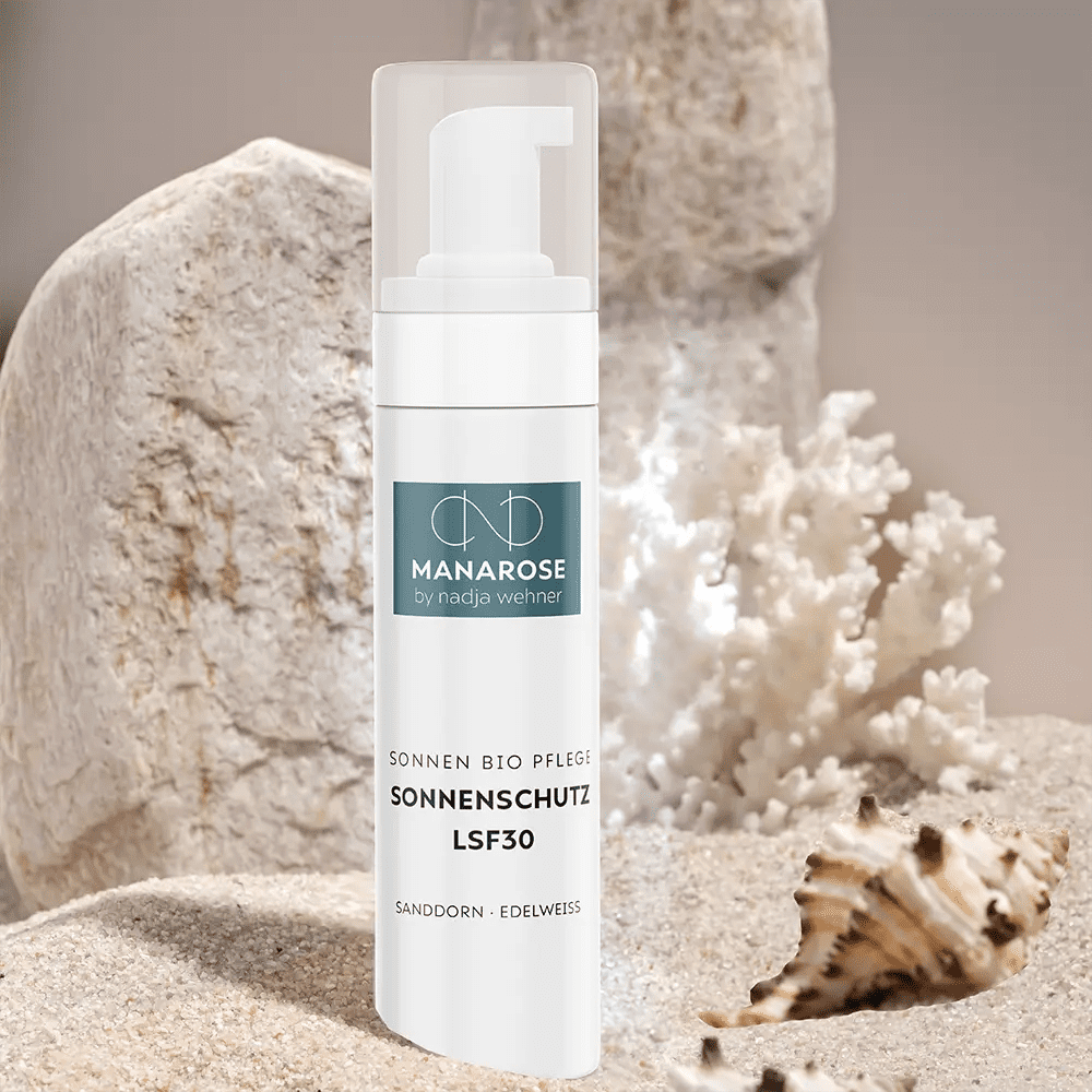Eine Flasche Sonnenschutz LSF 30 Sanddorn Edelweiß Sonnenschutzlotion von Manarose Biokosmetik an einem Strand mit Felsen und Sand, der natürlichen Schutz bietet.