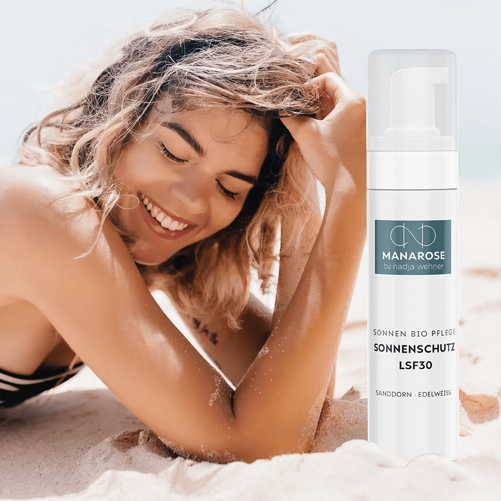 Eine Frau liegt mit einer Flasche Manarose Biokosmetik Sonnenschutz LSF 30 Sanddorn Edelweiß am Strand.