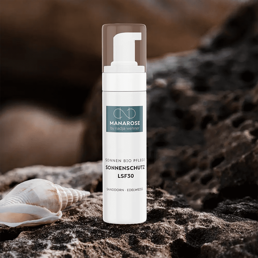 Eine Flasche Sonnenschutz LSF 30 Sanddorn Edelweiß von Manarose Biokosmetik mit einer Muschel auf einem Felsen, die natürlichen Schutz bietet.