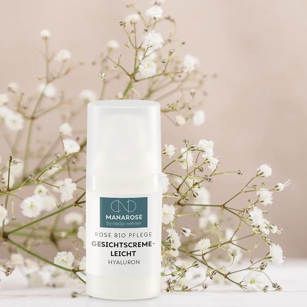 Eine Flasche Gesichtscreme Leicht Hyaluron von Manarose Biokosmetik auf einem Tisch mit weißen Blumen, die natürliche Pflege für geschmeidige Haut und strahlende Haut bietet.