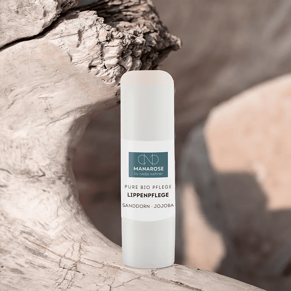 Eine Tube Lippenpflege Sanddorn Jojoba-Lippenbalsam aus natürlichen Luxus-Zutaten, auf einem Stück Holz sitzend, von Manarose Biokosmetik.