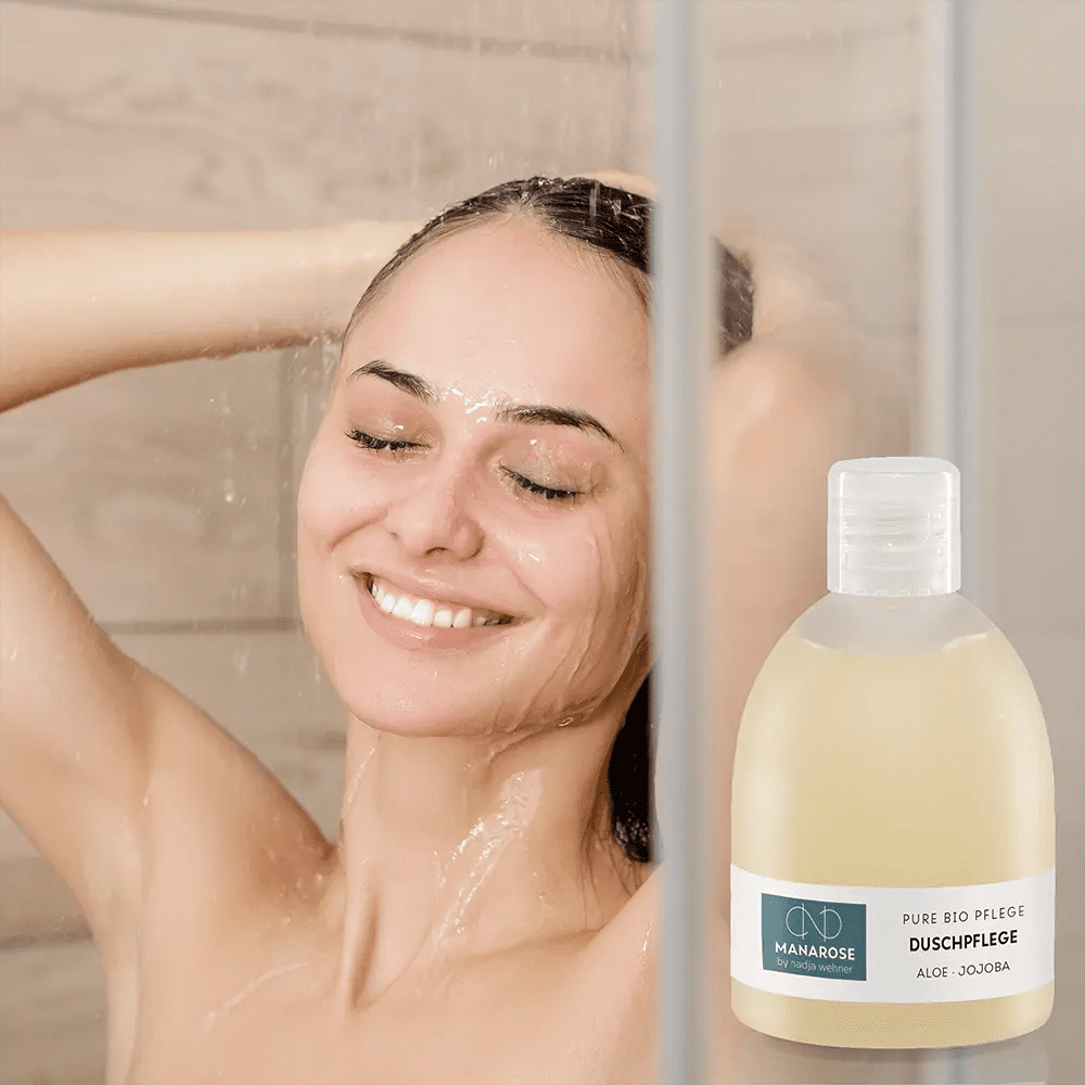 Eine lächelnde Frau vor der Dusche mit Duschpflege Aloe Jojoba von Manarose Biokosmetik und einer Flasche Duschgel.