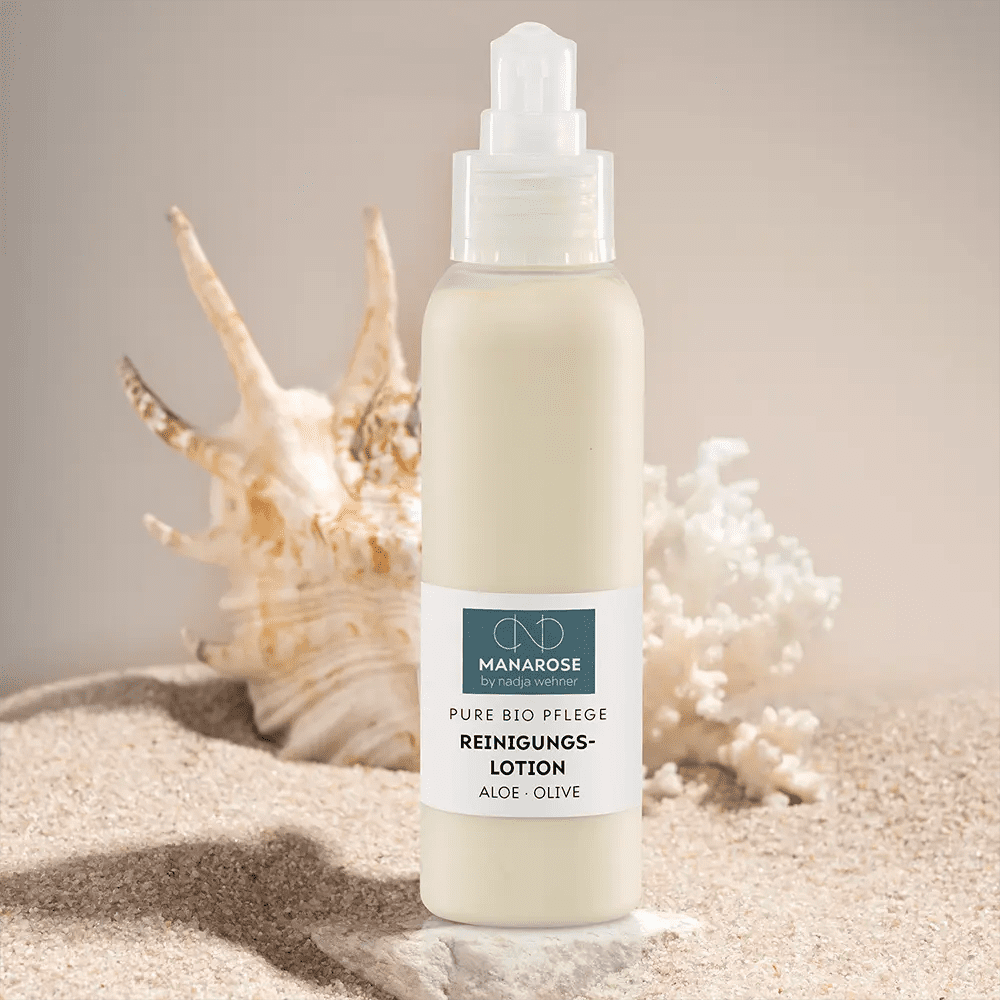 Eine Flasche Reinigungslotion für Hautpflege mit Aloe Vera-Extrakt und Muscheln am Strand, das Reinigungslotion Aloe Olive von Manarose Biokosmetik.