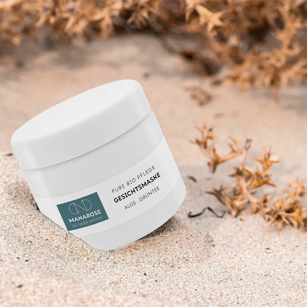 Ein Glas Manarose Biokosmetik Gesichtsmaske Aloe Grüntee-Creme sitzt auf dem Sand und spendet Ihrer Haut Feuchtigkeit.