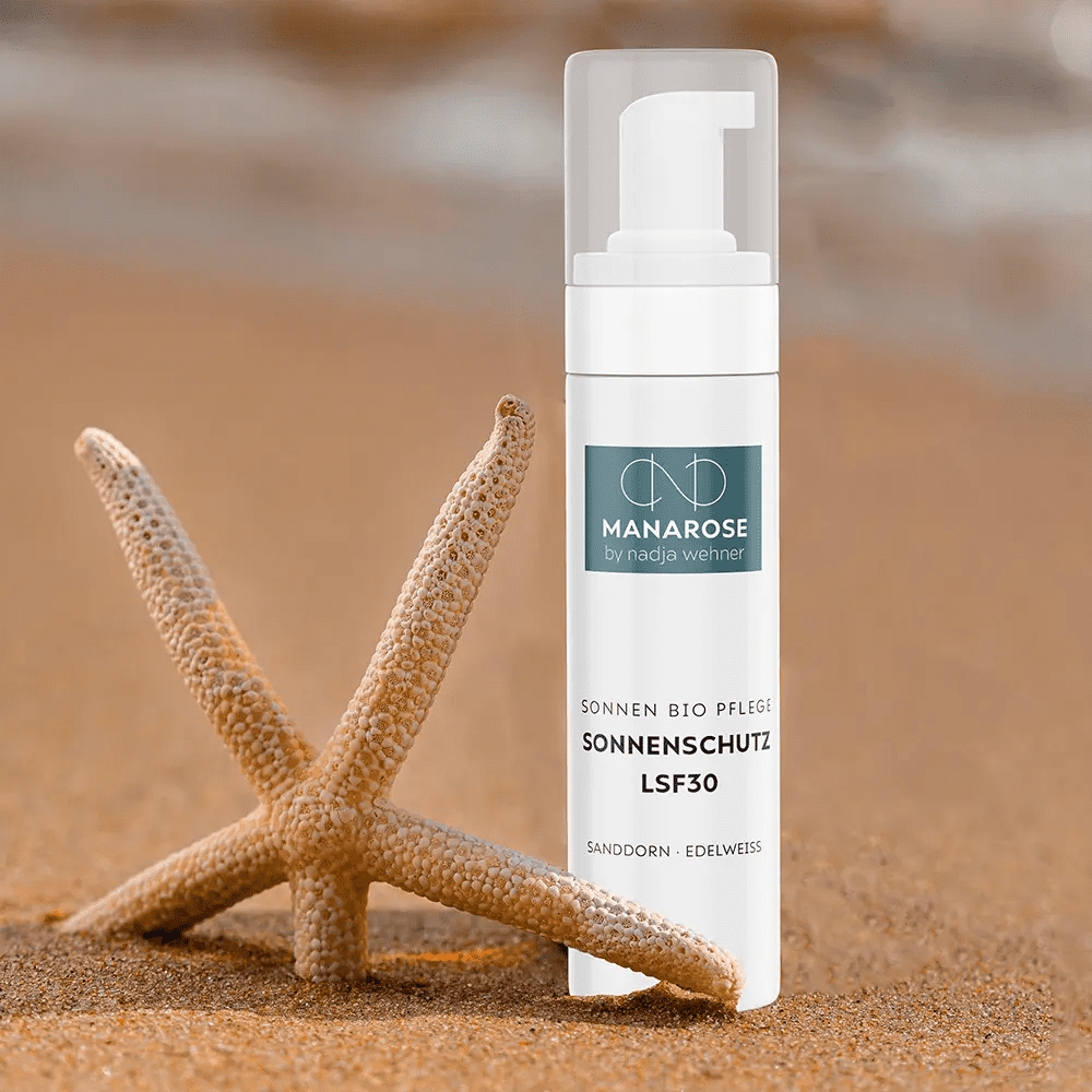 Eine Flasche Manarose Biokosmetik Sonnenschutz LSF 30 Sanddorn Edelweiß Feuchtigkeitslotion neben einem Seestern im Sand, der natürlichen Schutz bietet.