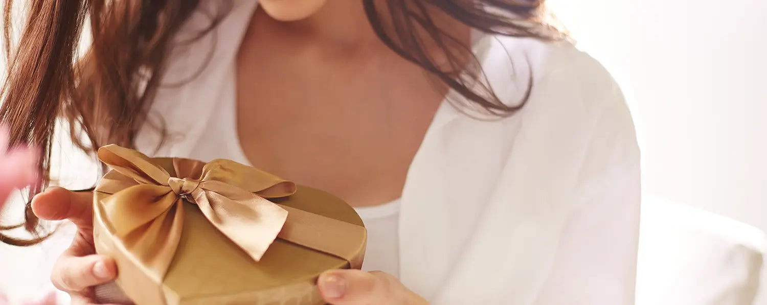 Eine Frau hält ein goldenes Geschenk in Form eines Herzes mit einer goldenen Schleife