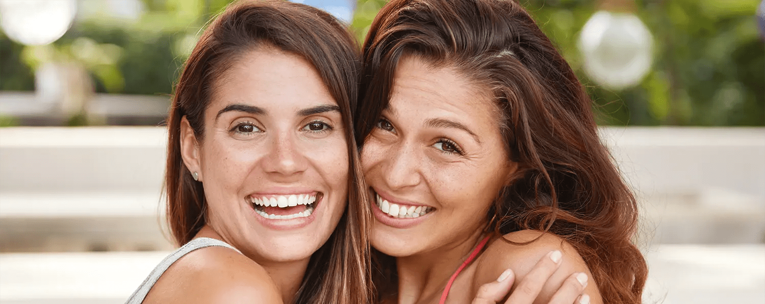 Zwei junge Frauen umarmen sich und lächeln in die Kamera