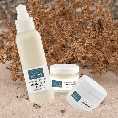 Ein Set von Manarose Biokosmetik Gesichtsreinigung Set – Perfect Skin-Produkten im Sand neben einer Pflanze.